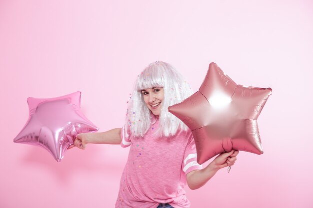 Funny Girl with silver hair gives a smile and emotion on pink background. Young woman or teen girl with balloons and confetti