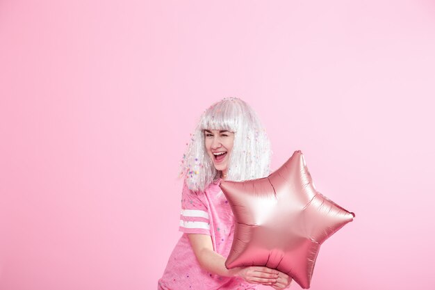 Funny Girl with silver hair gives a smile and emotion on pink background. Young woman or teen girl with balloons and confetti