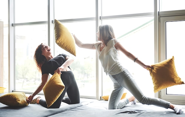 Free photo funny girlfriends play pillows, near large windows.