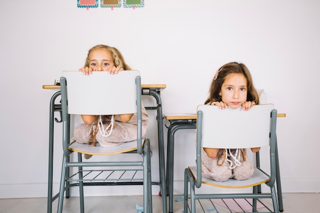 Funny girls peeking from behind chairs