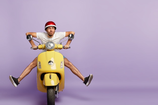 забавный парень в шлеме за рулем желтого скутера
