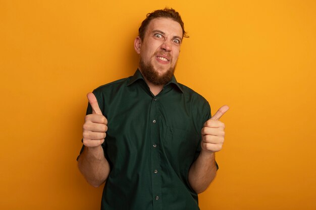 Забавный красивый белокурый мужчина показывает палец вверх двух рук, изолированных на оранжевой стене