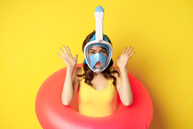 Funny happy woman in swimming ring wearing snorkling mask for diving posing against yellow background