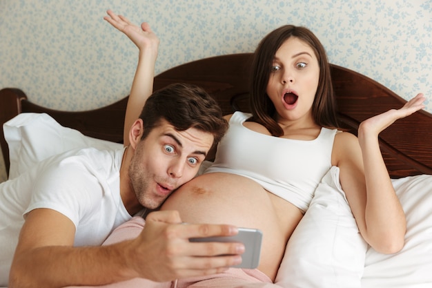 Funny happy young pregnant couple taking selfie Free Photo