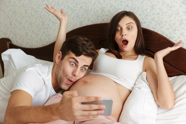 Смешные счастливые молодые беременные пары принимая селфи