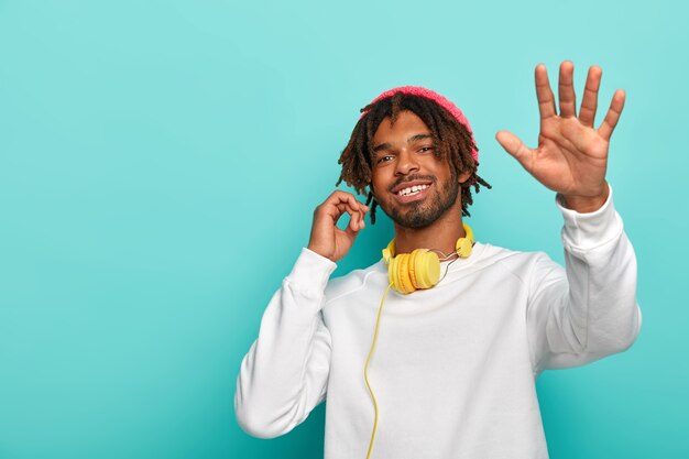 Funny hipster man dances, uses stereo headphones, isolated over blue background, copy space.