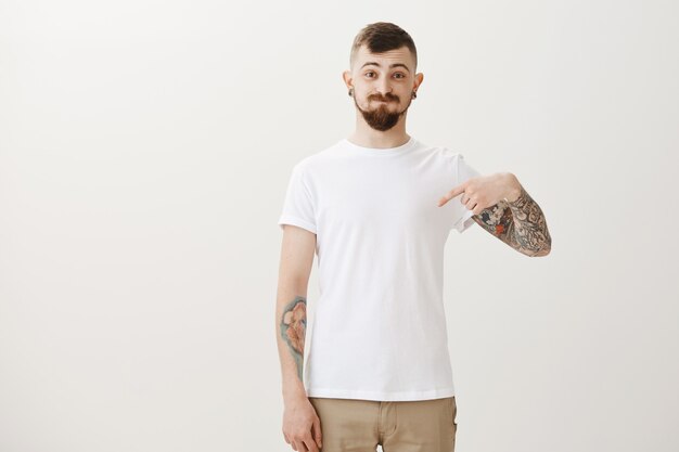 Funny hipster student with tattoos pointing finger down and pouting silly