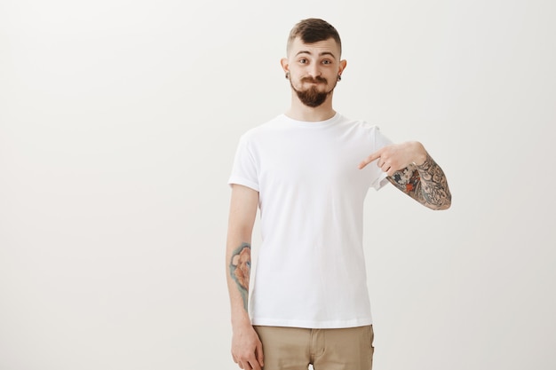 Funny hipster student with tattoos pointing finger down and pouting silly