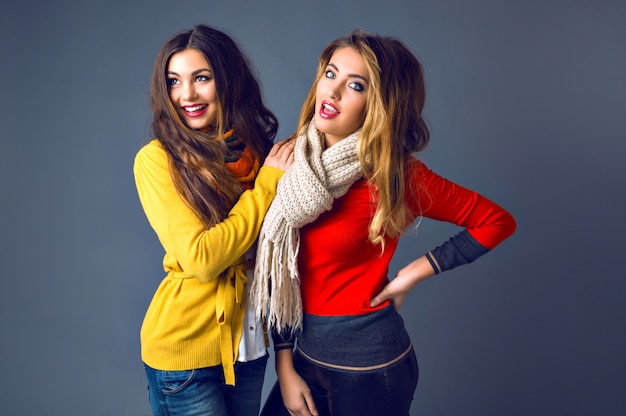 Funny indoor portrait of who hipster girls having fun in studio, wearing classic cashmere sweaters and scarfs