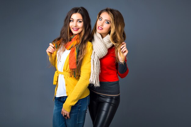 Funny indoor portrait of who hipster girls having fun in studio, wearing classic cashmere sweaters and scarfs