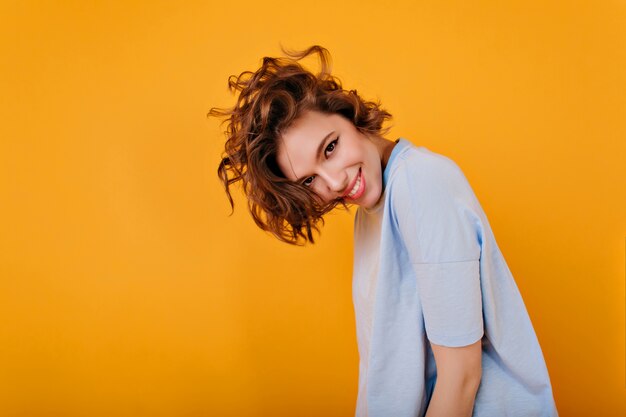 Funny inspired girl with brown hair playfully posing on yellow space