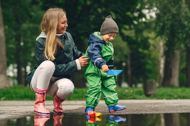 Забавный малыш в резиновых сапогах играет в дождевом парке