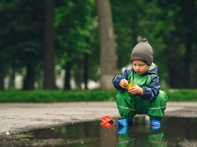 Bambino divertente in stivali da pioggia che giocano in un parco di pioggia