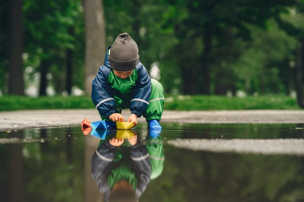 Funny kid in rain boots playing in a rain park