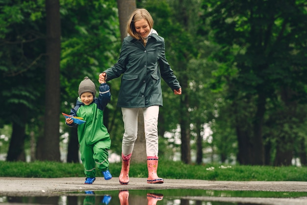 Funny kid in rain boots playing in a rain park