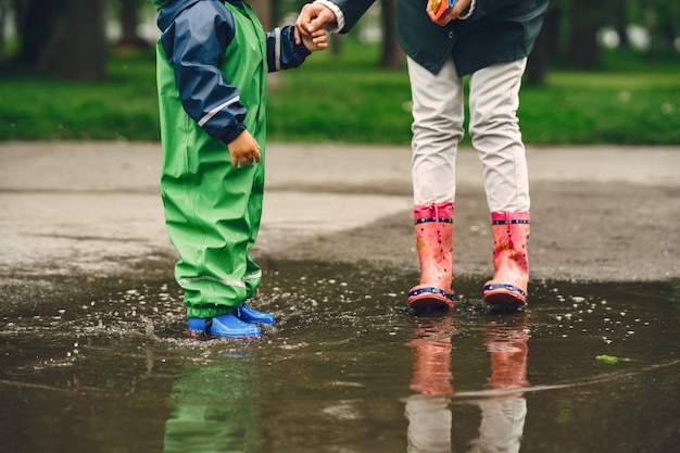 Funny kid in rain boots playing in a rain park