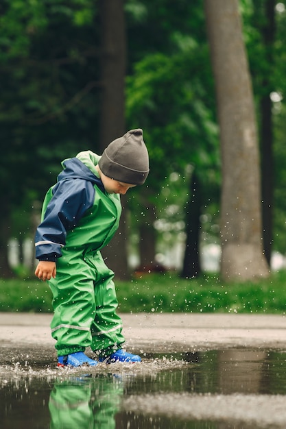 Bambino divertente in stivali da pioggia che giocano in un parco di pioggia