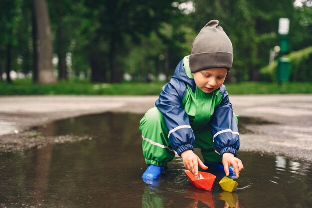 Funny kid in rain boots playing in a rain park