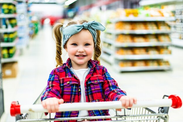 Funny little child girl, sitting in the trolley during family shopping in hypermarket