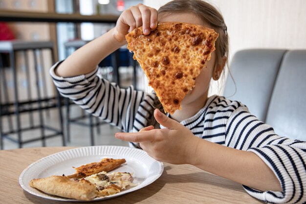 Funny little girl eating cheese pizza for lunch close up.