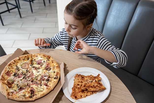 Funny little girl eating pizza in a cardboard box for lunch.