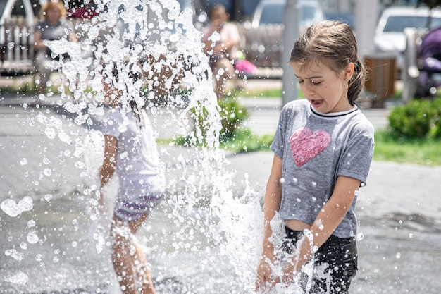 Смешная маленькая девочка в фонтане, среди брызг воды в жаркий летний день.