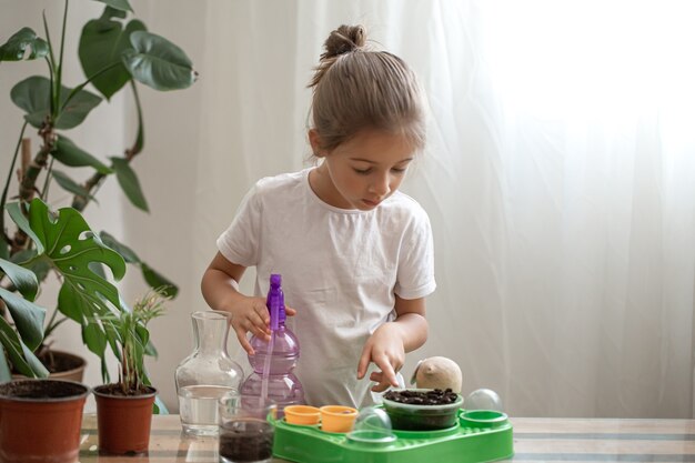 Funny little girl gardener with plants in the room at home, watering and caring for indoor plants, transplants flowers.