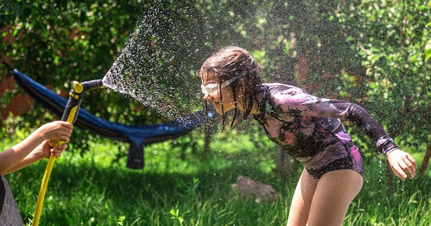 Бесплатное фото Забавная маленькая девочка, играющая с садовым шлангом на солнечном заднем дворе