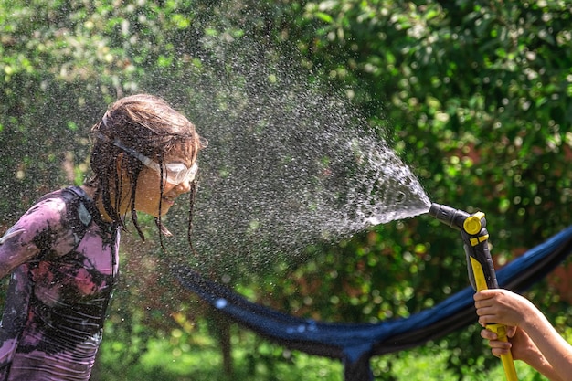 Бесплатное фото Забавная маленькая девочка, играющая с садовым шлангом на солнечном заднем дворе