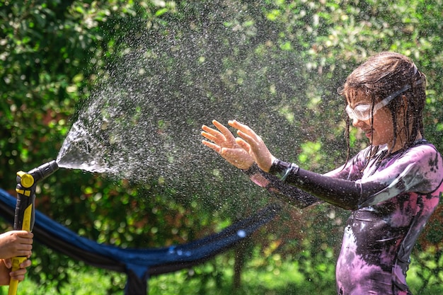 Ragazzina divertente che gioca con un tubo da giardino nel cortile soleggiato