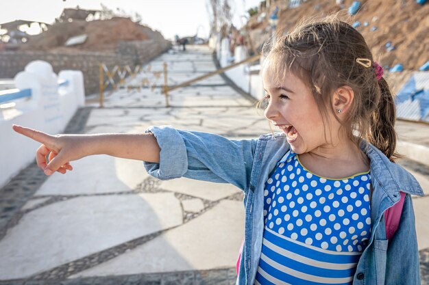 A funny little girl saw something interesting in the distance and points there.