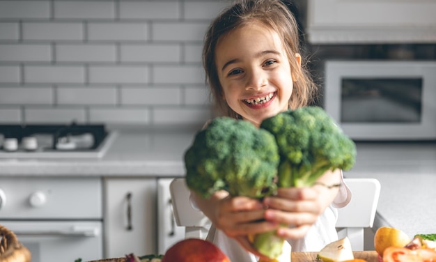 Бесплатное фото Смешная маленькая девочка с брокколи на кухне