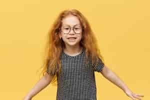 Free photo funny little girl with long loose red hair jumping expressing true positive emotions smiling broadly wearing large round spectacles. picture of cute cheerful child having fun posing isolated