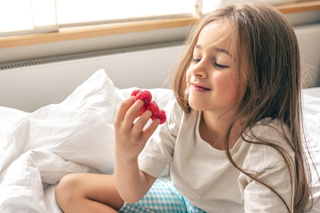 Funny little girl with raspberries on her fingers in bed in the morning