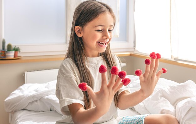 Funny little girl with raspberries on her fingers in bed in the morning