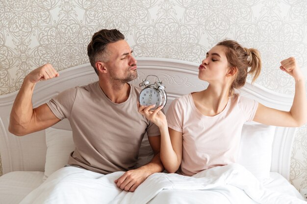 Funny Lovely couple sitting together on bed with alarm clock