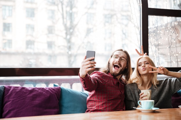 Le coppie amorose divertenti che si siedono in caffè fanno un selfie.