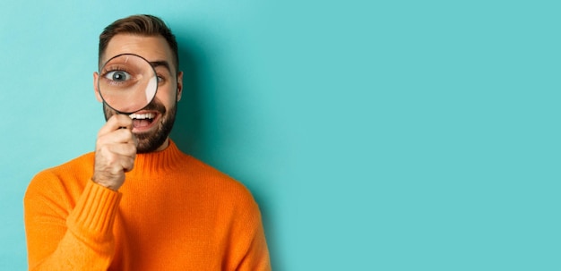 Free photo funny man looking through magnifying glass searching or investigating something standing in orange s