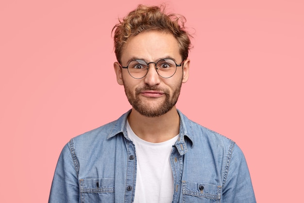 Funny man makes grimace, pouts lips, has comic facial expression, curly hair, bristle