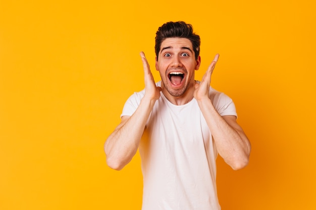 Funny man in white outfit shouts joyfully and looks enthusiastically at camera on orange space