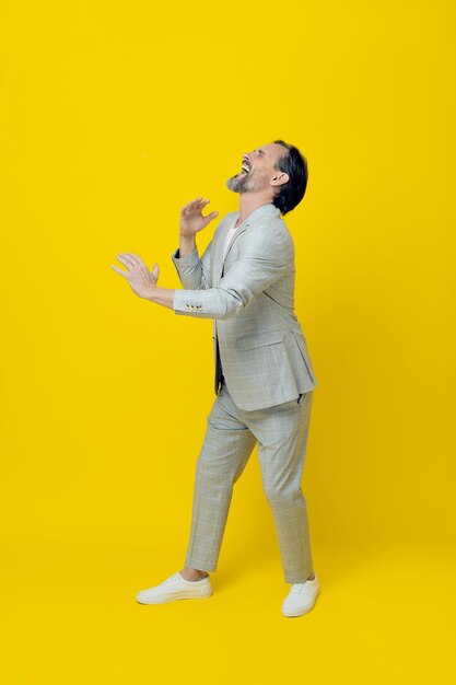 Забавный деловой человек средних лет притворяется, что играет на саксофоне, смеясь с закрытыми глазами на желтом фоне Красивый зрелый бизнесмен в белом костюме Бизнес-концепция Копирование пространства