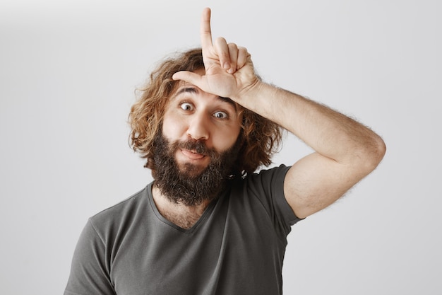 Free photo funny middle-eastern guy mocking person with loser sign on forehead
