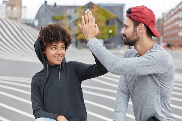 Funny mixed race teenagers with friendly expressions give high five to each other, agree doing something
