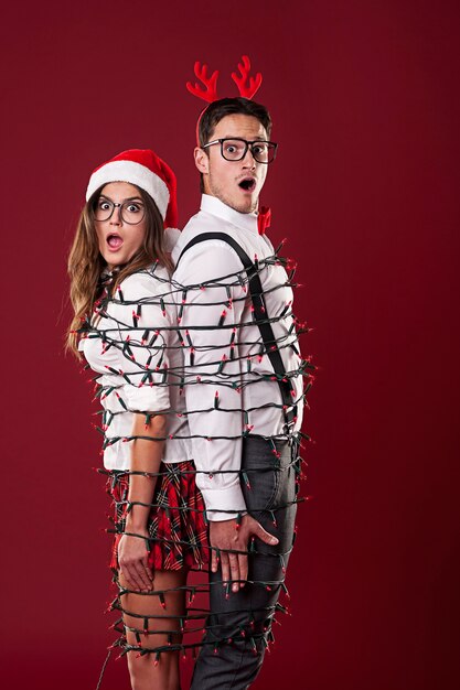 Funny nerd couple are tangling  in christmas lights