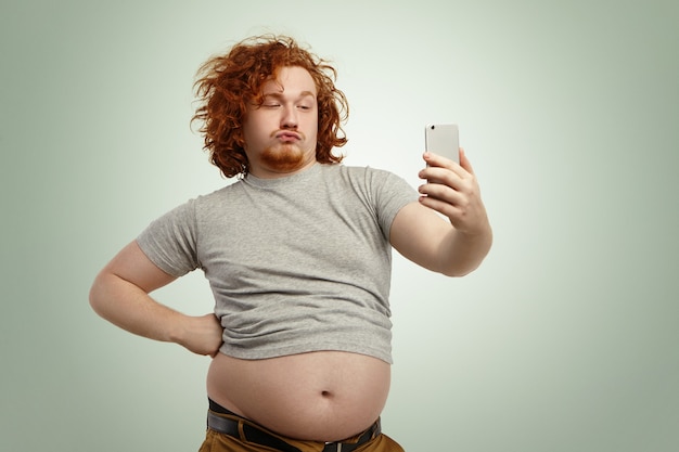 Funny overweight plump man with duck lips wearing undersize t-shirt with belly hanging out of pants