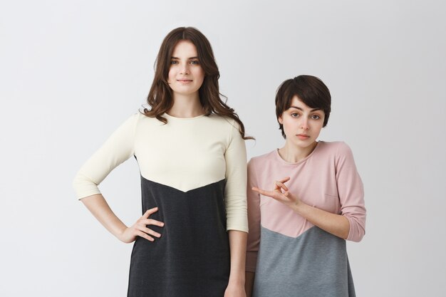 Funny portrait of lesbian pair of young student girls in matching clothes. Long-haired girl being taller than her short girlfriend.