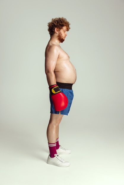 Funny redheaded man in blue boxing shorts and gloves isolated on gray