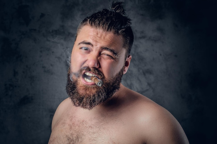 मुफ़्त फोटो funny shirtless bearded male smoking a cigar on grey background.