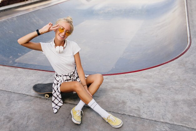 Funny skater woman with trendy hairstyle expressing positive emotions. Outdoor portrait of joyful female model chilling in skate park.