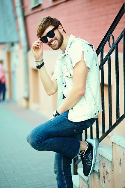 Смешной улыбающийся битник красавец парень в стильной летней одежде на улице в солнцезащитные очки
